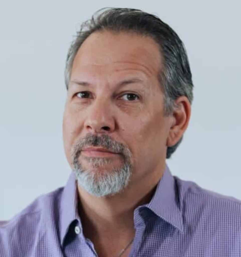 גבר בגיל העמידה, עם שיער קצר ומסורק לאחור, זקן תיש ושפם, לבוש בחולצה סגולה עם צווארון, מביט למצלמה על רקע בהיר וחלק — ספי דורי מומחה בטיפול רגשי במשברי חיים.