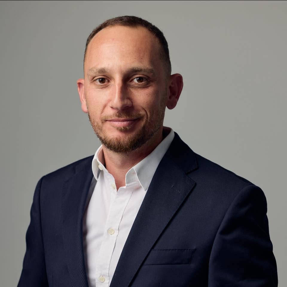 שניר נפתלי, עורך דין לענייני משפחה, עם שיער קצר וזקן מסודר, לובש ז'קט כחול כהה וחולצה לבנה, מצולם על רקע אפור בהיר.