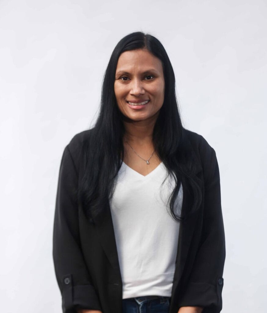 שירן לשם, מומחית ליווי פיננסי, עם שיער שחור ארוך לבושה בחולצה לבנה ובלייזר שחור, עומדת מול רקע לבן וחיוך על פניה.