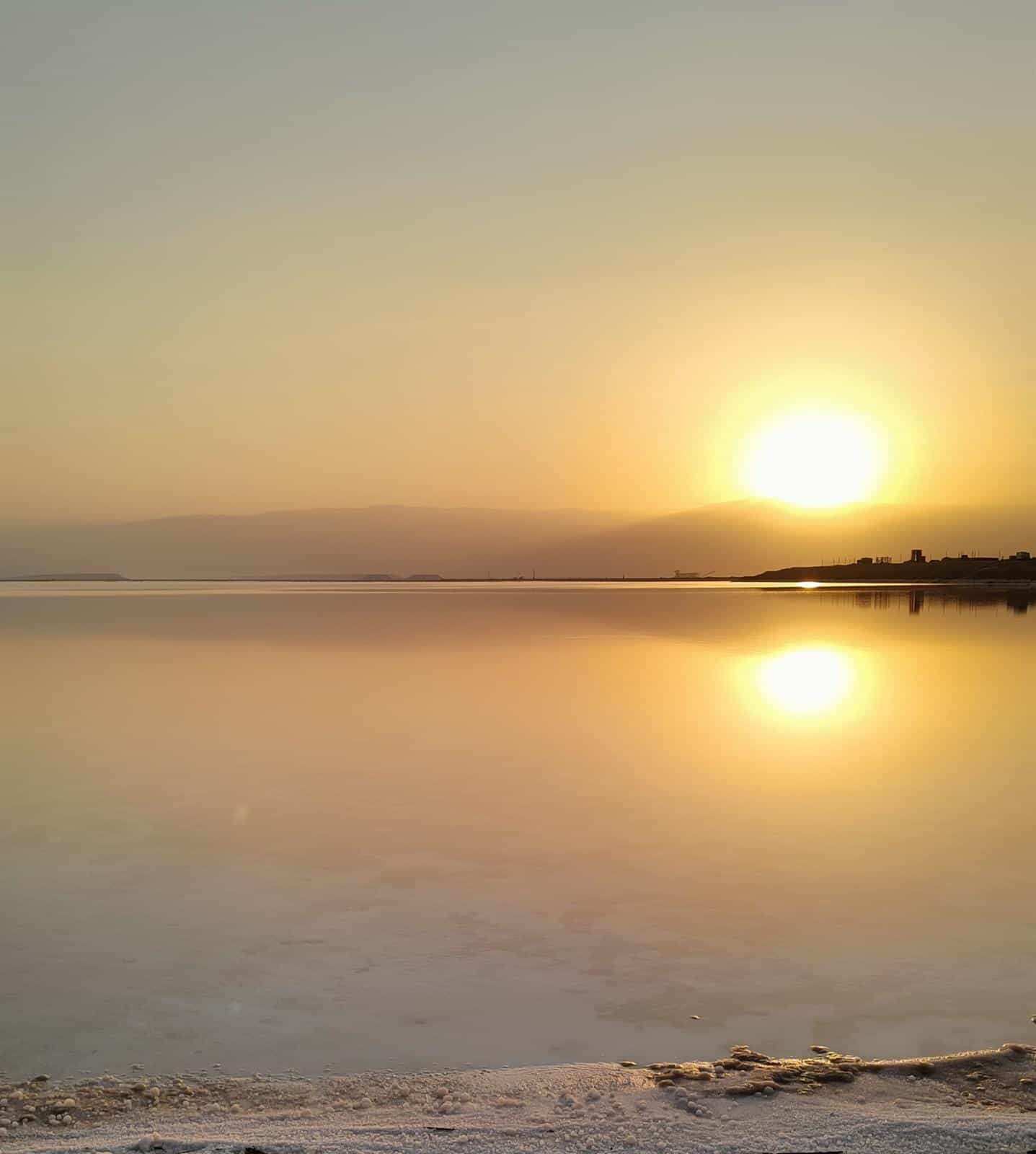 מים רגועים משקפים את השמש השוקעת ואת השמיים המעורפלים, עם קו חוף חול בקדמת התמונה — תמונה המעוררת הרהורים שקטים, בדומה לרגעים המוקדשים ללמידה איך להתמודד עם פרידה וגירושין.