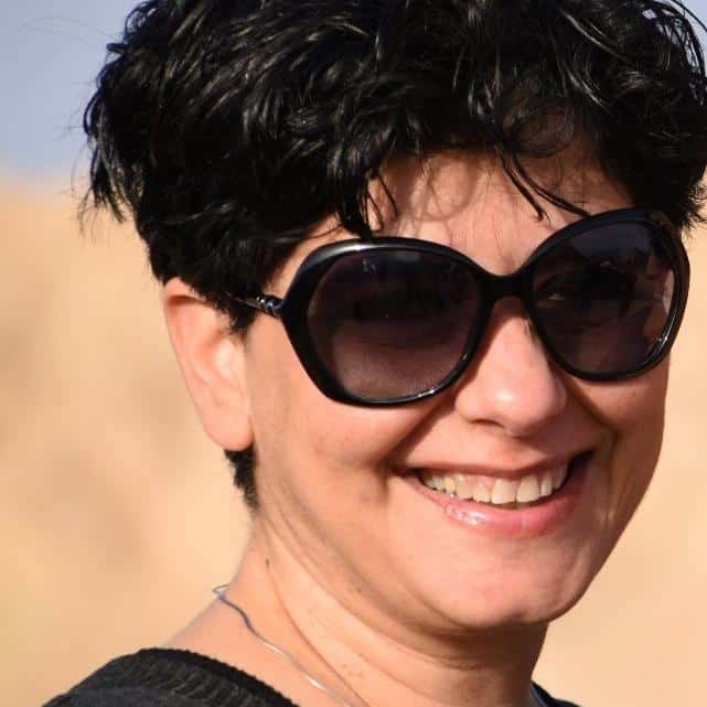 אדם עם שיער קצר וכהה ומשקפי שמש גדולים מחייך בחוץ, על רקע בז' מטושטש — מגשרת ועו"ד אסתי חומסקי נהנית מיום בהיר.