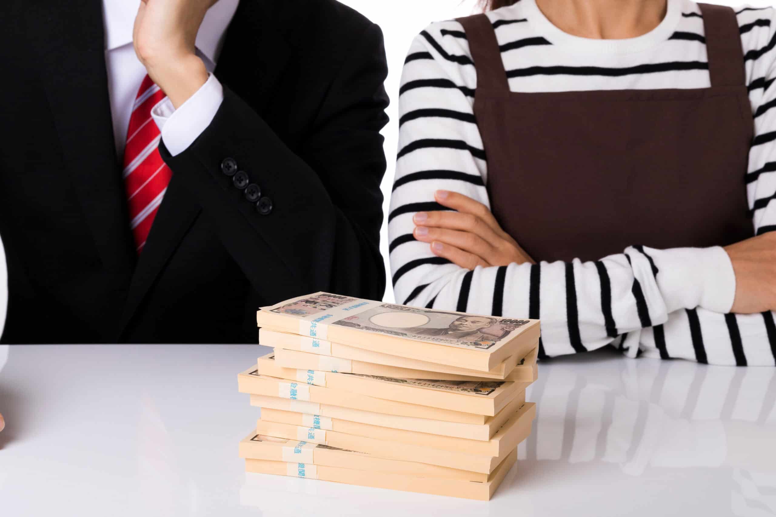 שני אנשים יושבים ליד שולחן, זרועותיהם שלובות, מול ערימת שטרות ין יפני — מתארים את הפחד הכלכלי מגירושין ברוח "עצמאות חדשה" של אורלי רובין. רק פלג גופם העליון נראה.